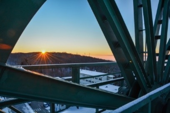 Foto eines winterlichen Sonnenaufgangs, fotografiert durch die Speichen eines großen Metallrads.