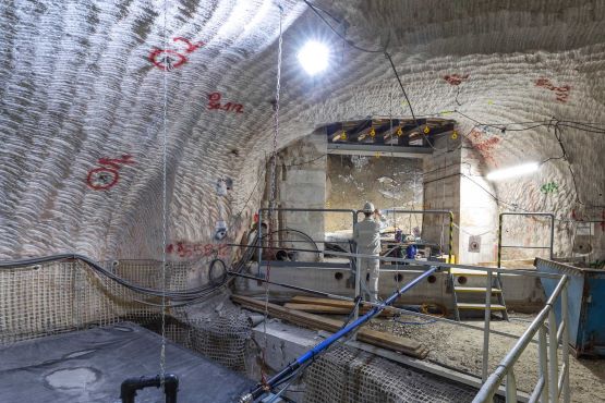 A brightly illuminated cavity underground: on the left of the picture is a reservoir; it is surrounded by a metal railing. In the background is a miner in white work clothes.