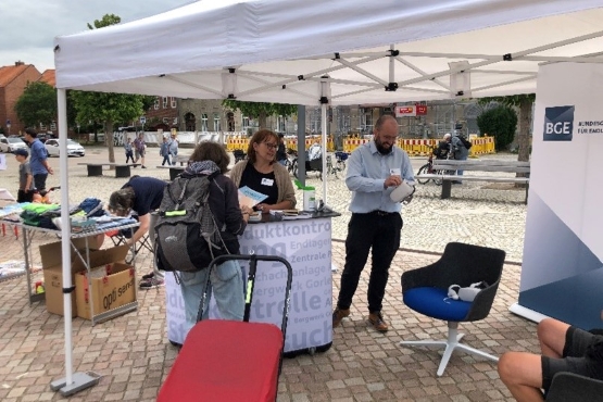 Das Bild zeigt mehrere Personen, die unter einem Pavillon stehen und sich miteinander unterhalten. Auf einem Drehstuhl zwischen den Personen liegt eine VR-Brille.