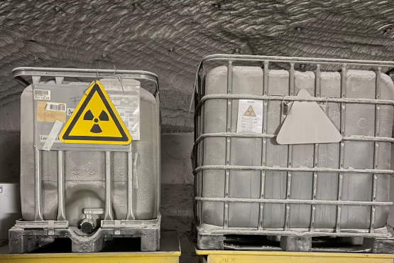 Zwei graue Behälter stehen auf zwei gelben Behältern. Auf dem einen grauen Behälter befindet sich ein Symbol des Flügelrads in einem Dreieck. 