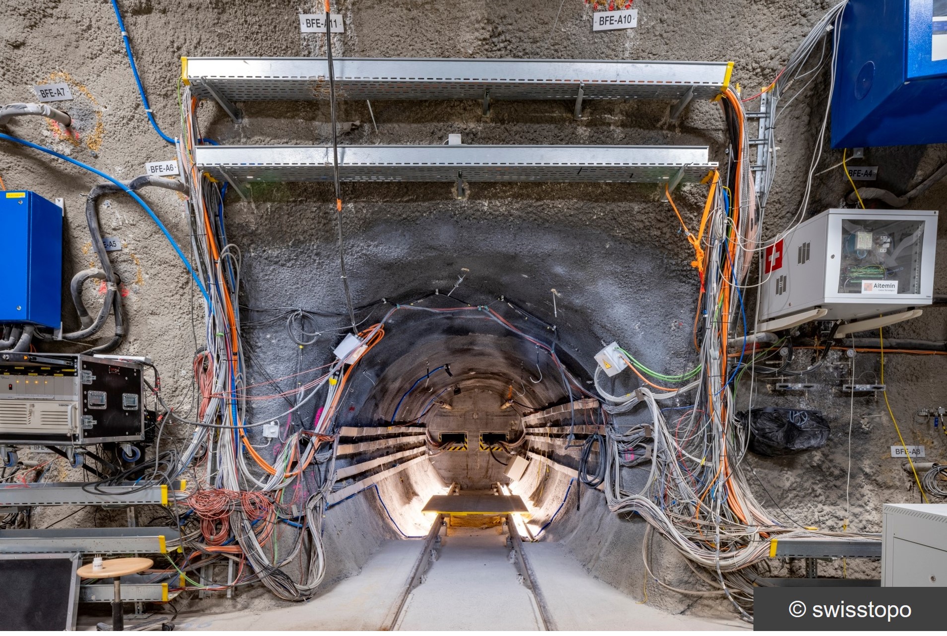 Das Foto zeigt den Tunnel des FE-Experimentes im Felslabor Mont Terri, Schweiz. Der Tunnel ist mit zahlreichen Messgeräten und Sensoren ausgestattet. Aus dem Inneren des Tunnels verlaufen viele Kabelstränge zu Aufzeichnungsgeräten.