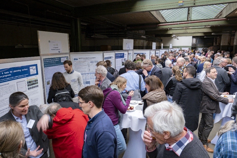 Zu sehen sind zahlreiche Menschen zu sehen, die sich Poster mit wissenschaftlichen Inhalten ansehen und darüber diskutieren.