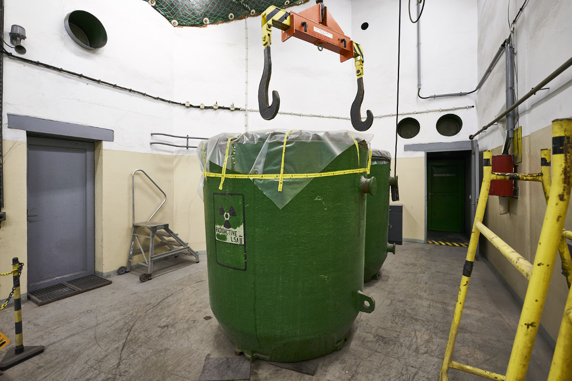 Im Dekontaminierungsraum stehen zwei große grüne Transportbehälter. Darüber sind die Haken einer Kranbahn zu sehen.