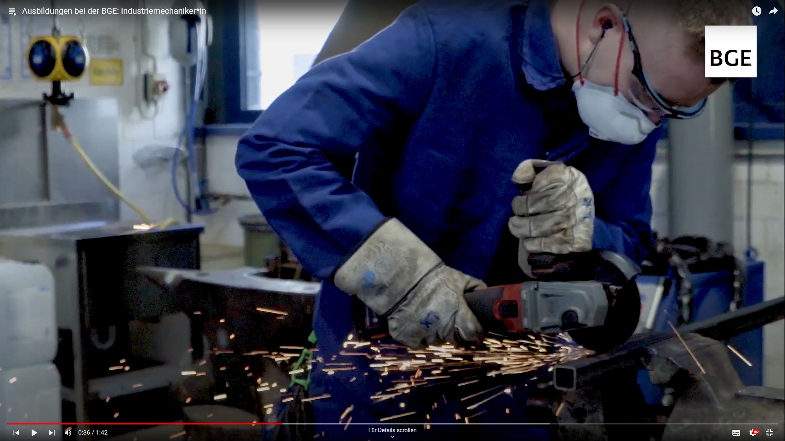 Das Foto zeigt einen Industriemechaniker in blauer Arbeitskleidung und Schutzbrille, der mit einem Trennschleifer ein Metallprofil bearbeitet. Es fliegen Funken.