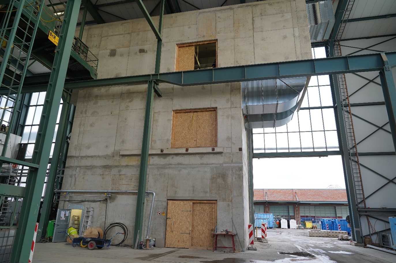 Das Foto zeigt die Druckluftanlageneinhausung; ein graues Gebäuse mit Holztüren in einer Industriehalle