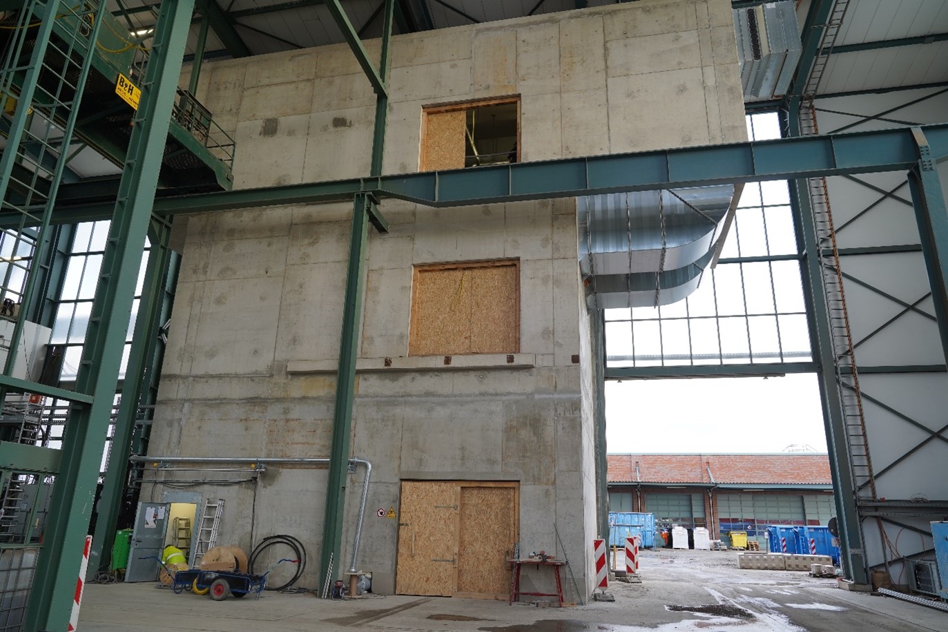 Die Druckluftanlageneinhausung in der Schachthalle von Konrad 1 Das Foto zeigt die Druckluftanlageneinhausung; ein graues Gebäuse mit Holztüren in einer Industriehalle