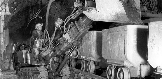 Die historische Aufnahme zeigt einen Bergmann der mit einem Schaufellader einen Förderwagen mit Erzgestein belädt