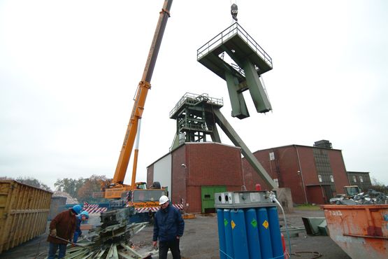 A crane lifts a detached element of an old winding tower