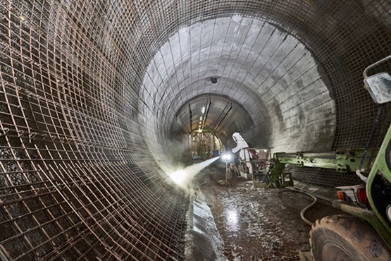 Ein Bauarbeiter im Schutzanzug spritzt Beton auf eine vorbereitete Wandfläche.