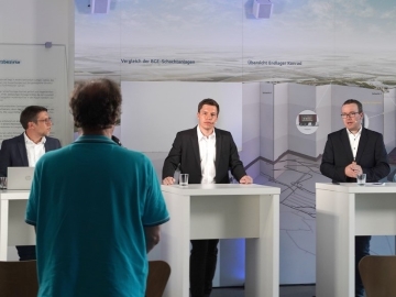 ) Eine Person richtet innerhalb einer Veranstaltung eine Frage an die Referierenden.