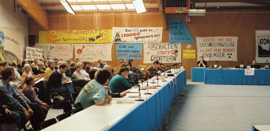 Eine Gruppe von Personen sitzt in einer Halle mit Protest-Transparenten im Hintergrund. Link zur Seite "Die Genehmigung des Endlagers Konrad"