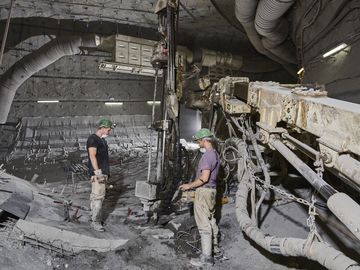 Two miners drill holes in the ground with a large machine for rock bolts