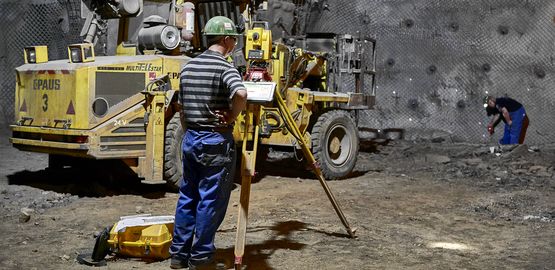 An employee stands underground at the future washing station in front of a measuring device. Link to page "Background information"