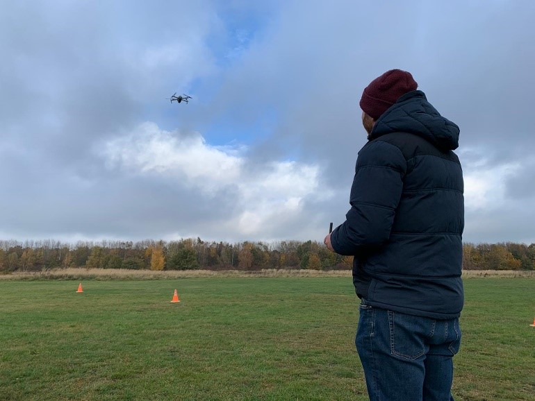 Eine Person lenkt mit einer Fernsteuerung eine Flugdrohne über ein Feld.