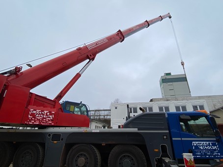 20220304_Anlieferung Autokran_2_Pixel Im Vordergrund steht ein roter Baukran. Im Hintergrund stehen Bürocontainer und das Mehrzweckgebäude der Schachtanlage Bartensleben.
