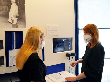 Zwei Frauen stehen vor einem kleinen Bildschirm in einem Ausstellungsraum