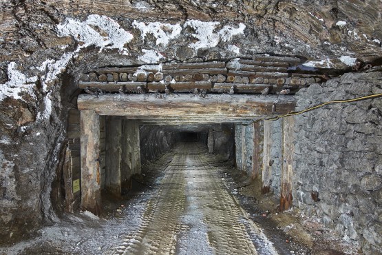 Ein Tunnel im Salzgestein unter Tage. Eine Holzkonstruktion besthend aus senkrechten und waagerechten Holzbalken stützt einen Teil der Decke des Tunnels. 