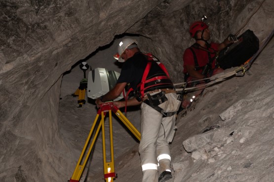 Zwei Männer in Klettergeschirr sind unter Tage – einer stellt einen Laserscanner auf