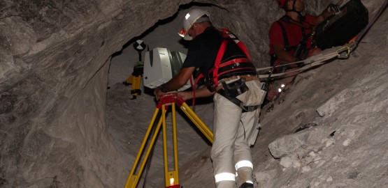 Two men in climbing harness underground – one sets up a laser scanner. Link to page "The work of the mine surveying team: pits, boundaries and geodata"